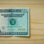 A twenty-dollar bill rests on a light wooden surface.