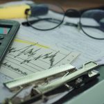 A desk with a calculator, papers, eyeglasses, and office supplies.